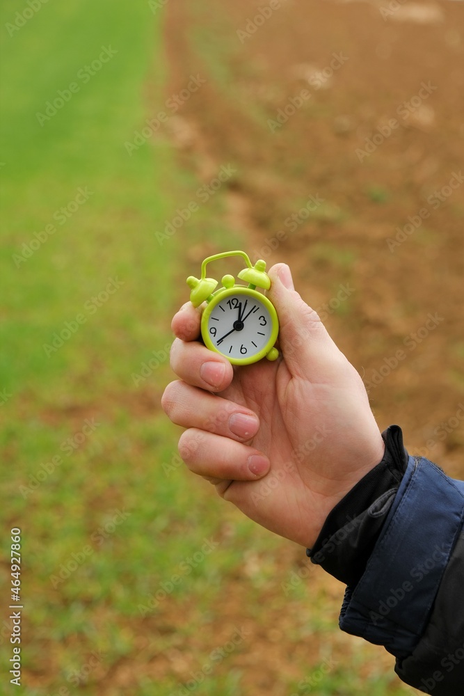 Spring planting time. Sowing time. Farming and agriculture concept. green and plowed field and a man's hand with a green alarm clock.Field work season.