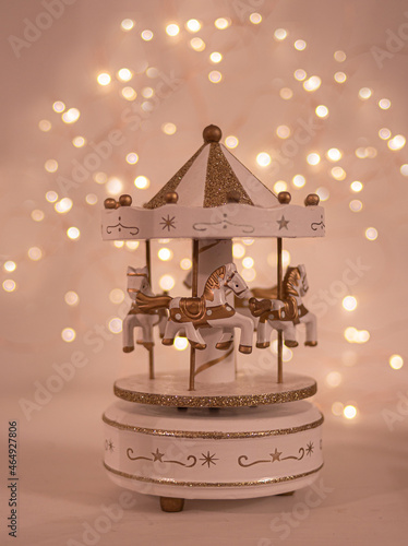 christmas festive scenery showing a musical box with golden carousel horses; front view with blurred bokeh lights background on white wooden table photo