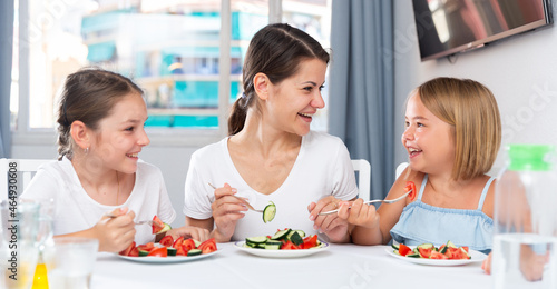 Mother with two daughters enjoying salad of fresh vegetables at the dinner table