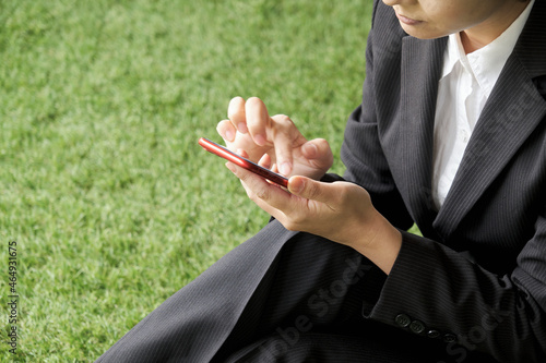 芝生の上に座ってスマートフォンを操作する女性 © apiox