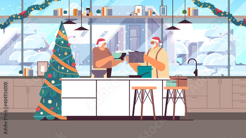 senior couple in santa hats cooking together in kitchen christmas dinner preparation new year holidays celebration concept