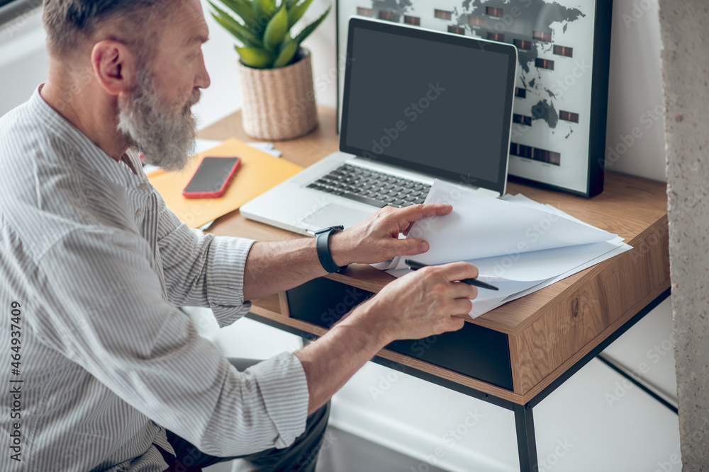 A mature businessman working from home and scrutinizing the documents A mature businessman working from home and scrutinizing the documents