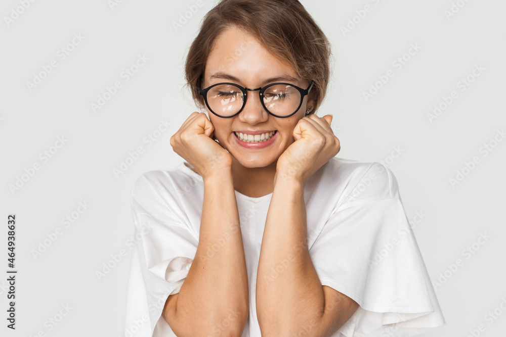 Young woman smiling at the camera on a white background. Portrait of a girl wearing glasses and holding her hands clenched in fists on her well-disposed face Young woman smiling at the camera on a white background. Portrait of a girl wearing glasses and holding her hands clenched in fists on her well-disposed face