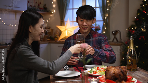 Happy young asian japanese couple with glasses of white wine having date at home kitchen during xmas eve. man and woman smiling making toast for love. celebrating christmas together