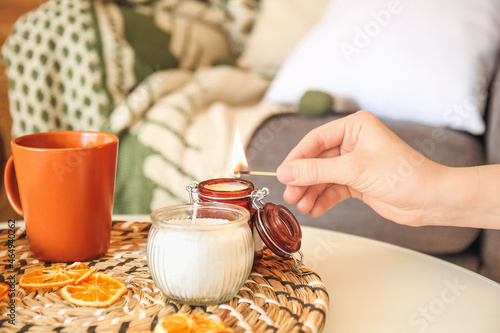 Woman lighting aroma candle on table in room