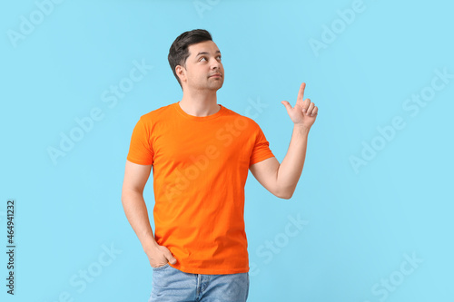 Handsome young man in stylish t-shirt pointing at something on color background