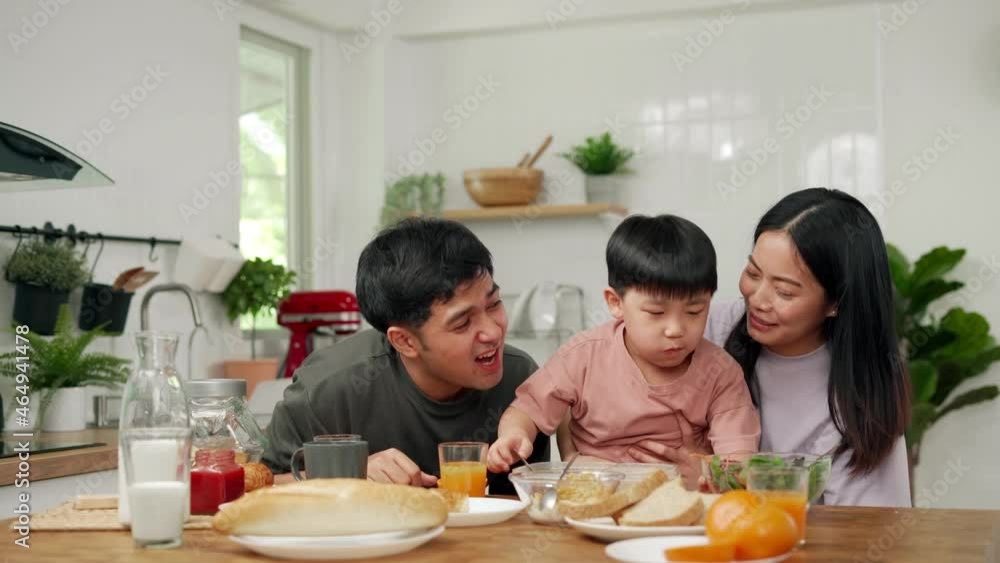 Asian family breakfast at home. Parents and children enjoy eating together, talking with laughter and good atmosphere. Father plays with son playfully at kitchen table. Asian family breakfast at home. Parents and children enjoy eating together, talking with laughter and good atmosphere. Father plays with son playfully at kitchen table.