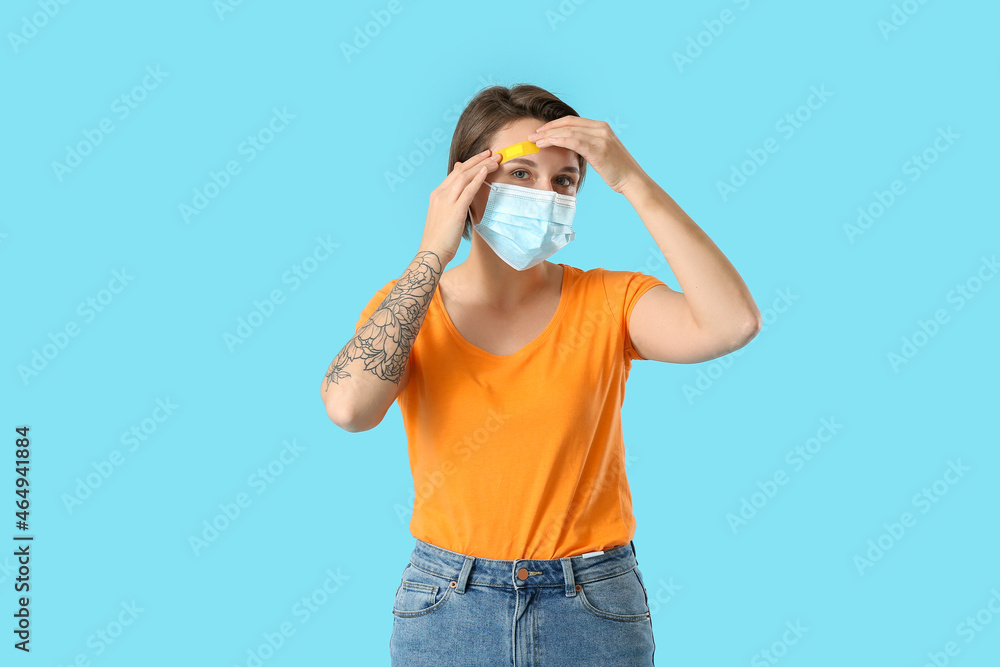 Young woman in medical mask applying plaster onto her forehead on blue background Young woman in medical mask applying plaster onto her forehead on blue background
