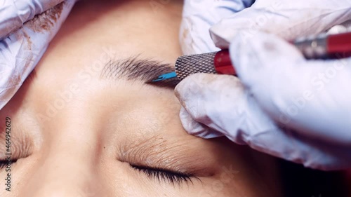 Close up microblading eyebrow tattoo. Beautician in gloves makes permanent makeup correction of the shape of the eyebrows to a young women. Eyebrow tattoo in a beauty salon.