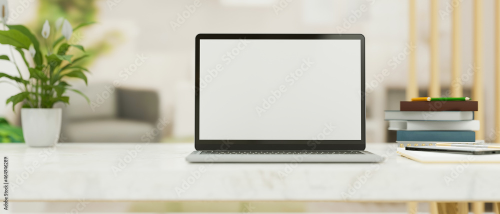 Fototapeta premium Modern white worktable with laptop mockup template with decor over blurred home living room in background.