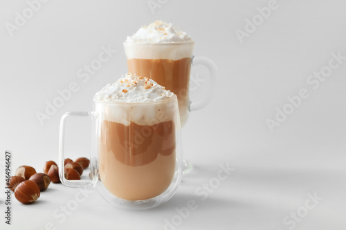 Glass cups of tasty latte with nuts on light background