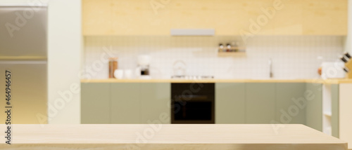 Modern light wooden kitchen counter island over blurred modern green and wooden kitchen interior.