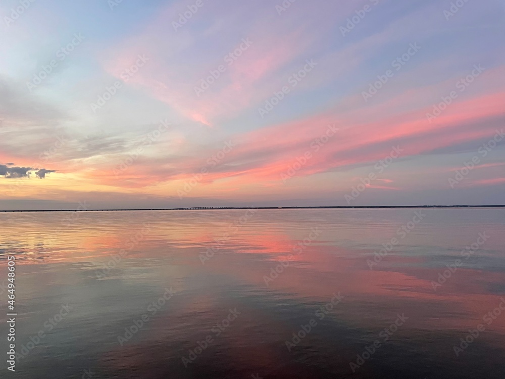 pastel sunset with reflections over calm bay water 