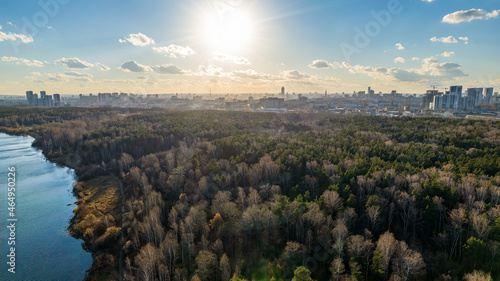 Autumn forest on lake shore at sunset and city on horizon  auerial view