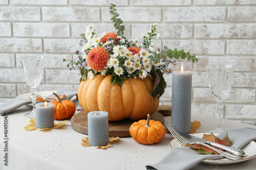 Beautiful bouquet of autumn flowers in pumpkin on served table near brick wall