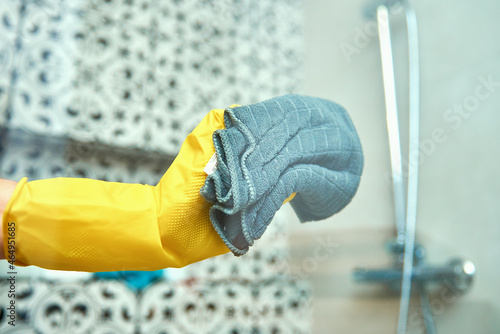 Woman in yellow rubber gloves cleans glass bathroom shower cabine. House cleaning