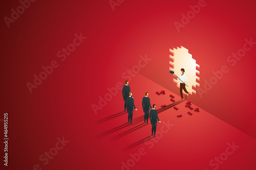 Businesswoman holding a hammer stands front group of businessmen on large wall.
