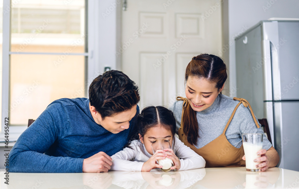 Portrait of enjoy happy love asian family father and mother with little asian girl smiling and having protein breakfast drinking and hold glasses of milk at table in kitchen