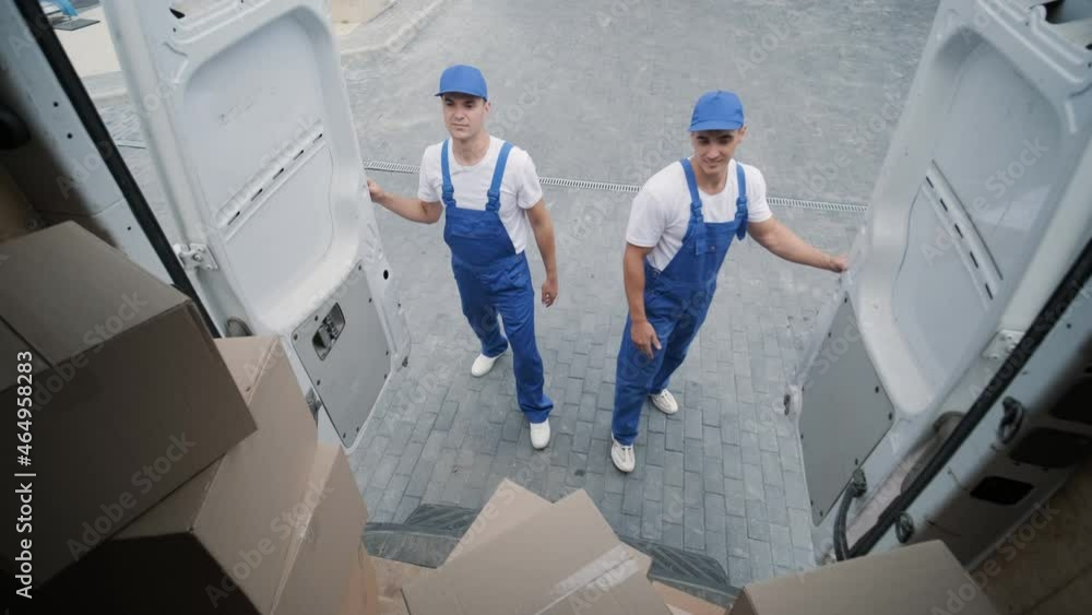 Two young workers of removal company unload boxes and furniture from minibus into customer's home Two young workers of removal company unload boxes and furniture from minibus into customer's home