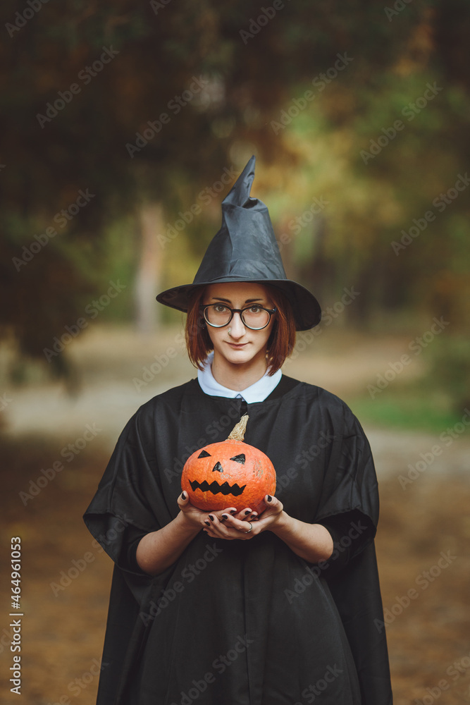 Halloween witch. Portrait of a girl in a hat and a witch costume with a pumpkin in the forest. Ready for the holiday