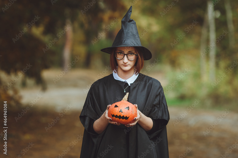 Halloween witch. Portrait of a girl in a hat and a witch costume with a pumpkin in the forest. Ready for the holiday