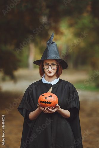 Obraz na płótnie Halloween witch. Portrait of a girl in a hat and a witch costume with a pumpkin in the forest. Ready for the holiday