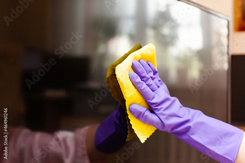 hand in a purple glove wipes the TV screen with a rag