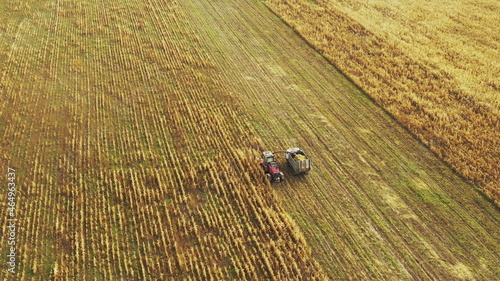 Aerial View Of Rural Landscape. Combine Harvester And Tractor Working In Corn Field. Collects Dry Corn Plants. Harvesting Of Maize In Late Summer. Agricultural Machine Collecting Plants In Cornfield