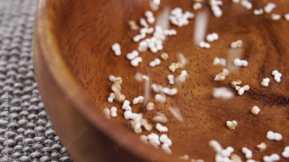 Popped dry amaranth falls into a rustic wooden bowl in slow motion on a jute cloth. Puffed pseudocereal grains. Macro Popped dry amaranth falls into a rustic wooden bowl in slow motion on a jute cloth. Puffed pseudocereal grains. Macro