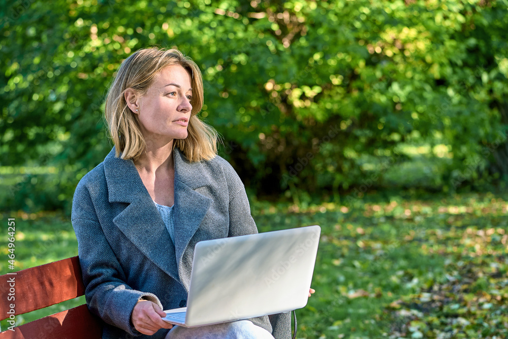 A woman with a laptop is sitting on a park bench A woman with a laptop is sitting on a park bench