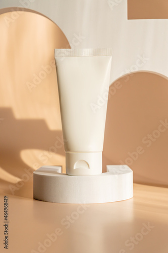 Beauty product concept. White tube of cream on beige backgrounds. Front view. Trendy showcase with hard light. Unbranded package.