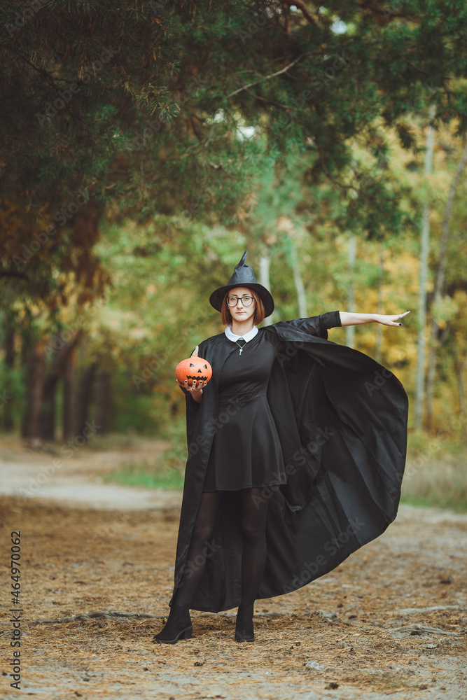 Halloween witch. Portrait of a girl in a hat and a witch costume with a pumpkin in the forest. Ready for the holiday