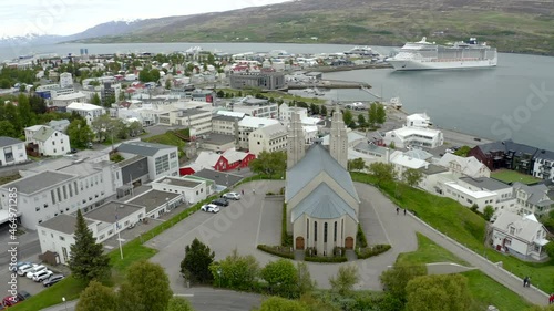 Half orbiting around Akureyrarkirkja church in Iceland revealing urban city scape. Cruise ship docked in port and revealing the whole city in background. photo