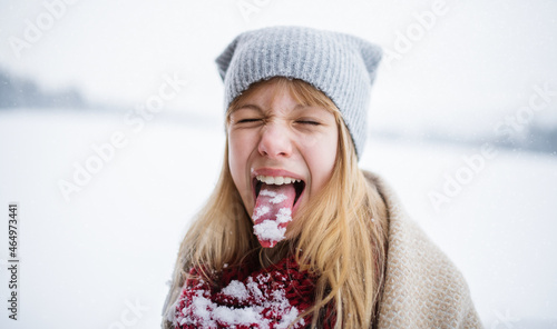 Headshot of happy preteen girl doing grimace and sticking tongue out with snow in winter nature photo