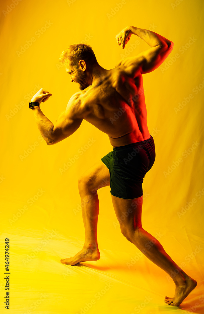 muscular man in blue shorts posing shows, straining his muscles. yellow and red highlights on the face and background