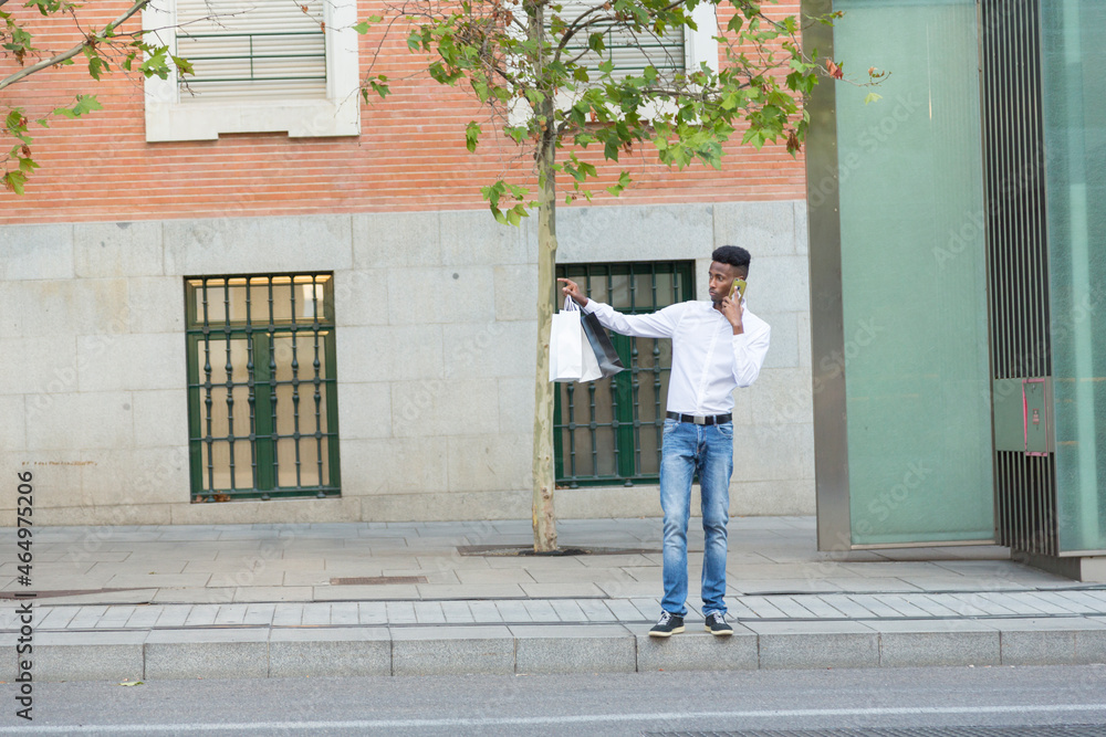 young afro man talking on the phone with paper bags in his hand hailing a taxi