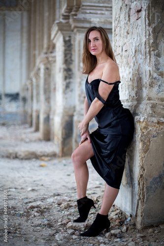 passionate female in a black dress stay near an old brick column in a dilapidated catholic church