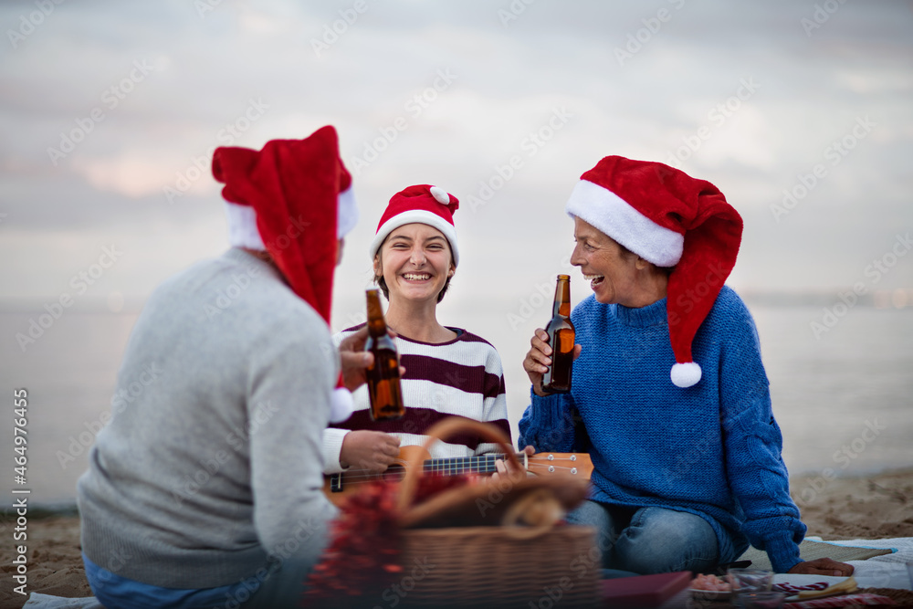 Fototapeta premium Senior couple with granddaugter with guitar celebrate New Year or Christmas and have picnic on beach.