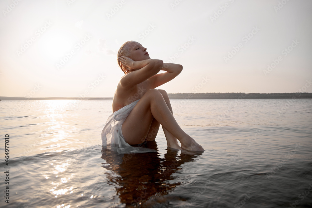 Wet Naked Beach Babes - Art nude sexy blonde with short haircut is sitting in water on shore beach  of lake at sunset. Wet hair and a woman body. Secluded beach holiday foto  de Stock | Adobe