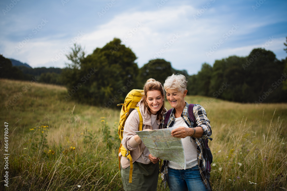 Happy mid adult woman with active senior mother hiking and looking at map outdoors in nature.