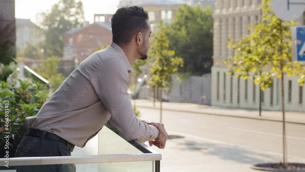 Side view portrait relaxed hispanic business man standing at railing modern skyscraper office building looking away on city street thinking resting. Close up successful guy male on balcony terrace Side view portrait relaxed hispanic business man standing at railing modern skyscraper office building looking away on city street thinking resting. Close up successful guy male on balcony terrace