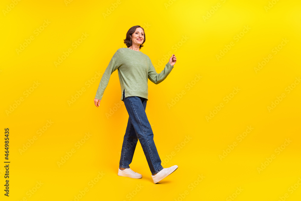 Full length body size view of attractive cheerful middle-aged woman strolling isolated over vibrant yellow color background Full length body size view of attractive cheerful middle-aged woman strolling isolated over vibrant yellow color background