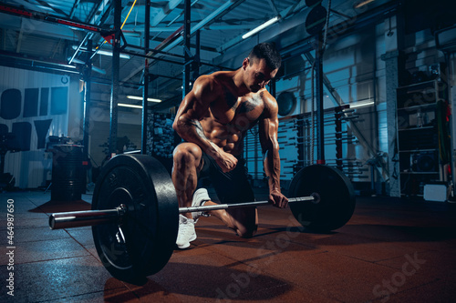 Young strong man, muscled athlete, bodybuilder training alone at sport gym, indoors. Concept of sport, activity, healthy lifestyle