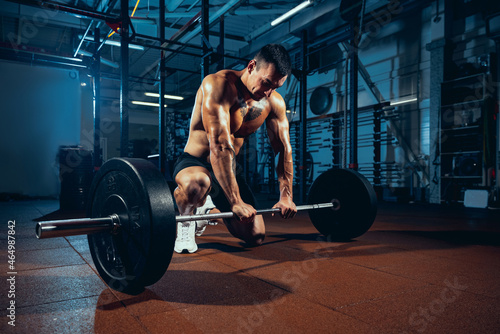 Young strong man, muscled athlete, bodybuilder training alone at sport gym, indoors. Concept of sport, activity, healthy lifestyle