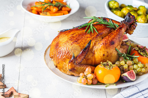 Roasted whole chicken served with fruits on plate, baked Brussels sprouts and carrots. Christmas or Thanksgiving food concept.