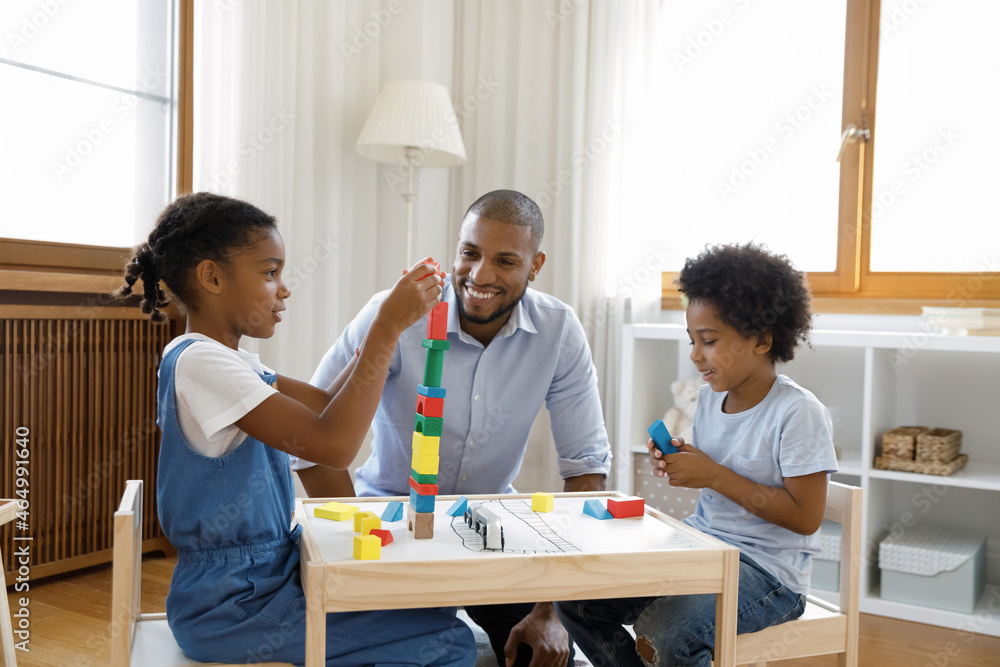 Happy affectionate young african american father playing toys with little children son daughter, constructing towers with cubes, sitting at table in modern living room, creative playtime concept. Happy affectionate young african american father playing toys with little children son daughter, constructing towers with cubes, sitting at table in modern living room, creative playtime concept.