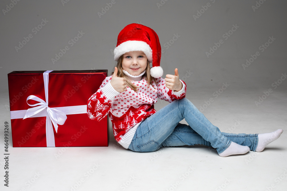 Obraz premium Lovely kid in Santa hat next to xmas gift.