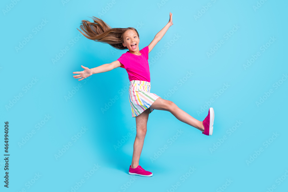 Full size photo of cheerful young amazed happy girl raise hands leg fly hair isolated on blue color background