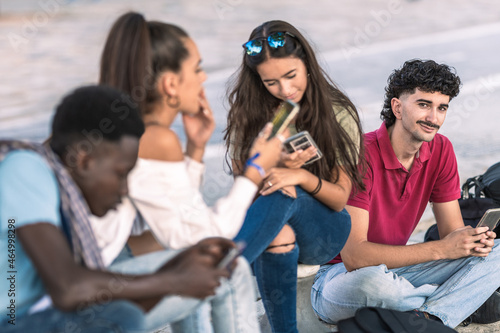Caucasian modern man sitting next to diverse group of friends using the mobile