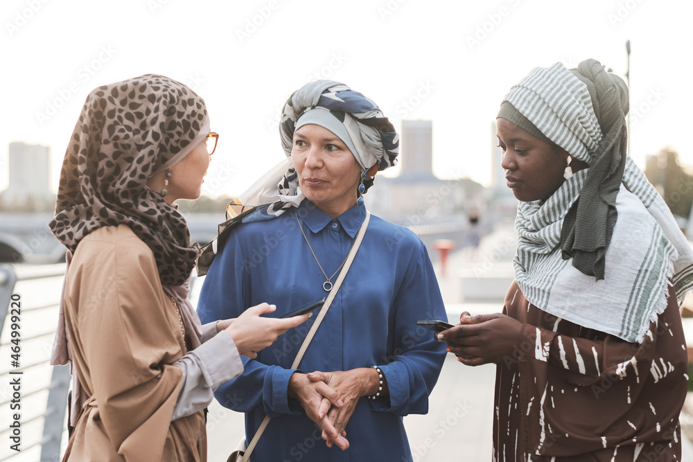 Group of muslim women using their mobile phones and discussing online apps while standing in the city